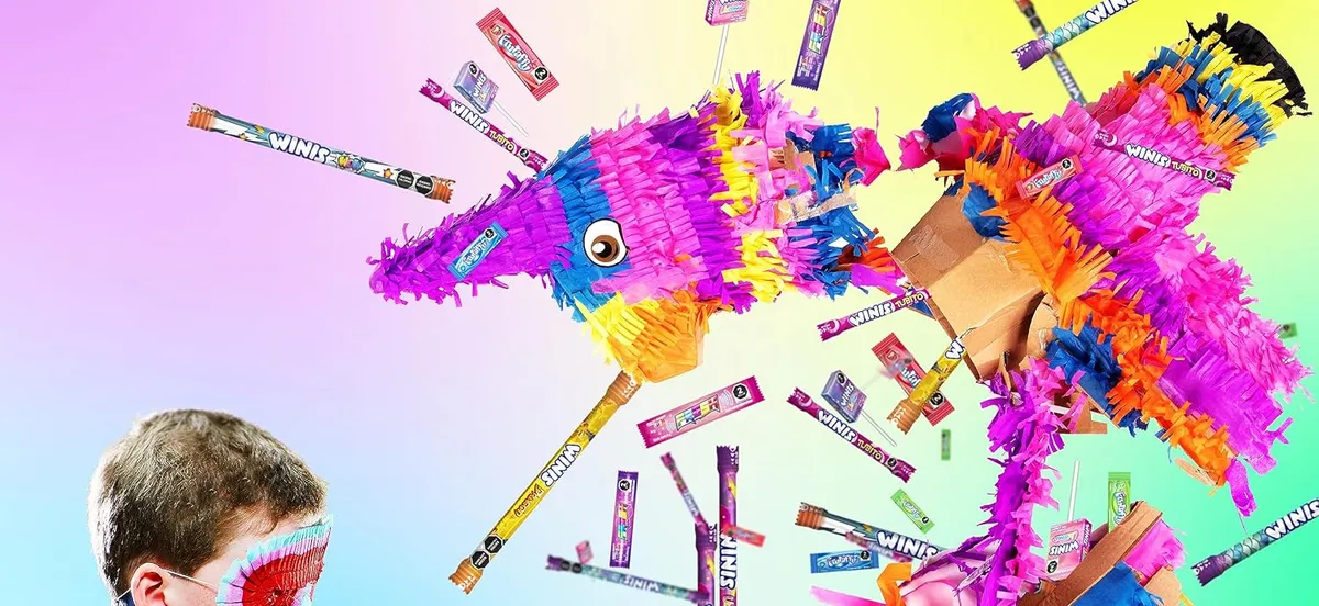 A boy in a blindfold swinging at a piñata as Winis candy sticks fly out